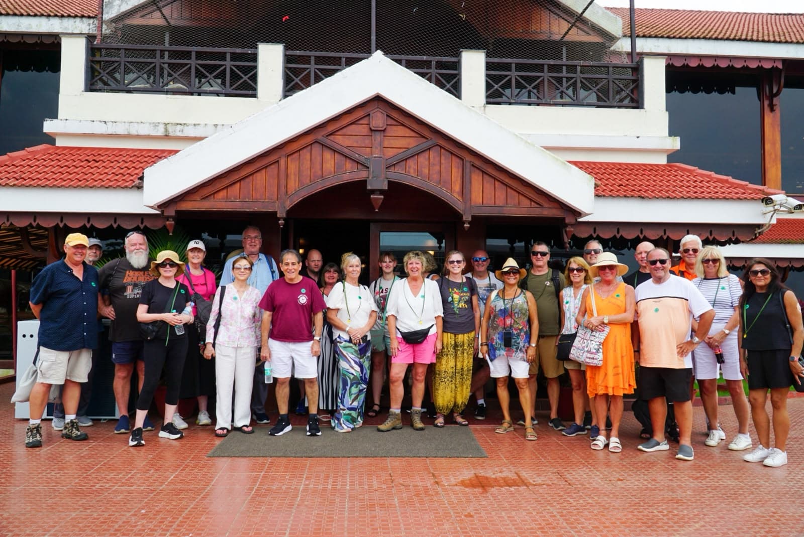 A large group of travellers posed together on the steps of a tile-roofed Kerala building.