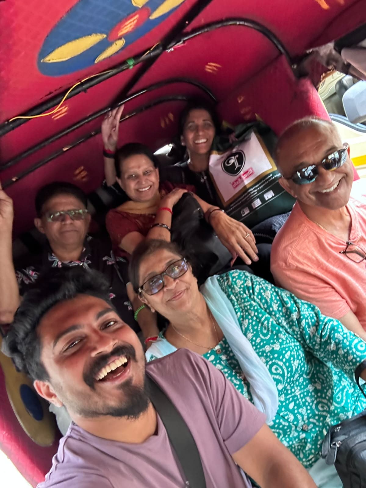 A group of travellers packed together and grinning on a ride, taken from the front.