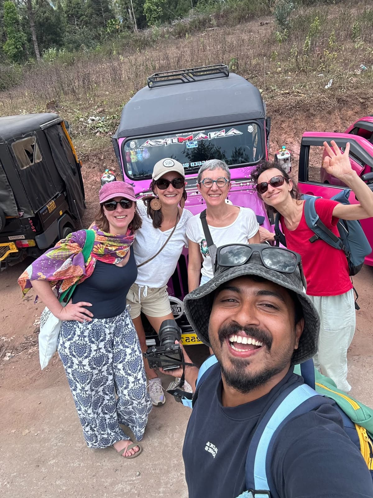 Travellers gathered beside off-road jeeps on a hill road, their guide in the foreground.