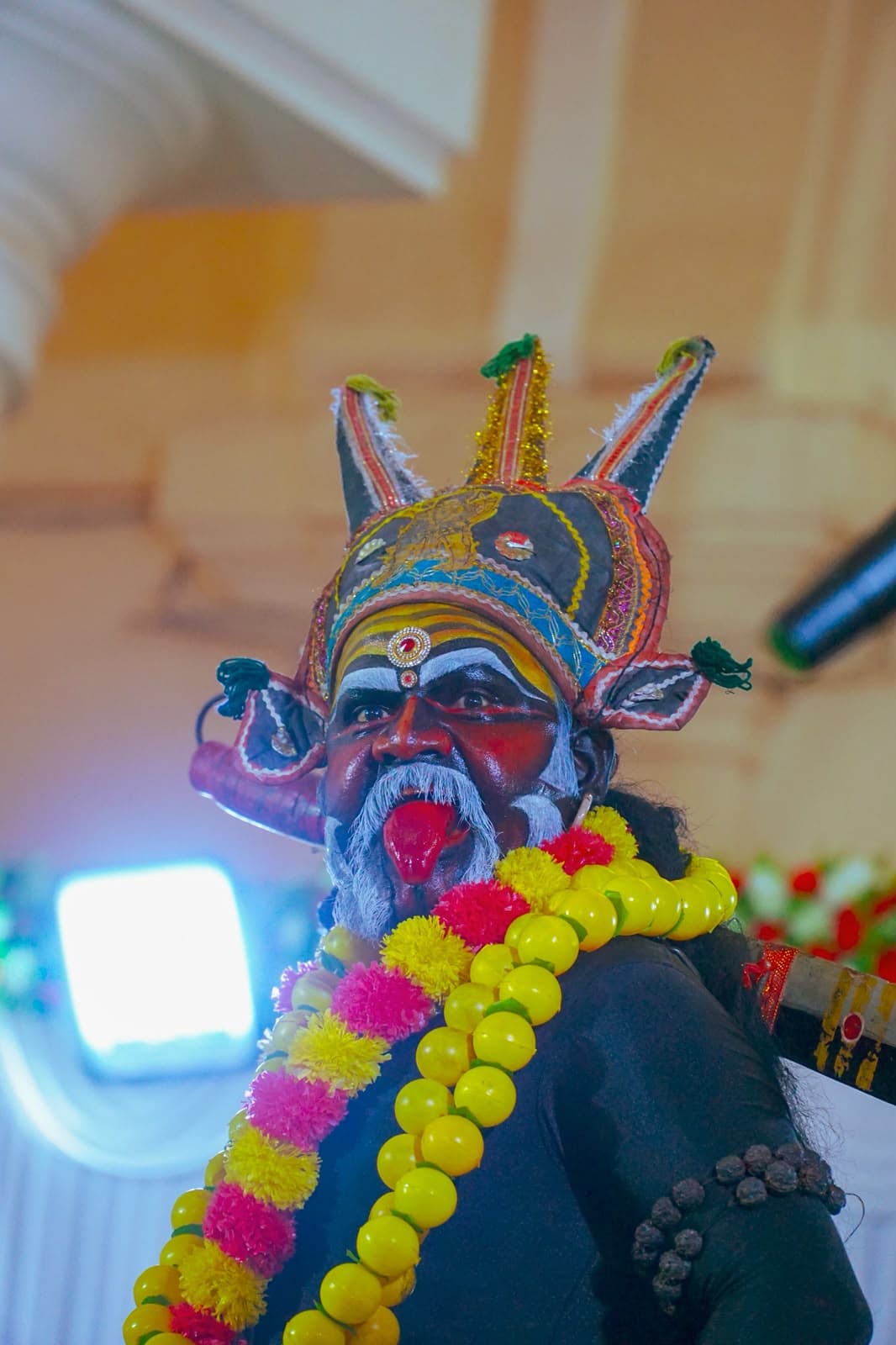 A Kathakali performer in painted face, headdress and marigold garlands.