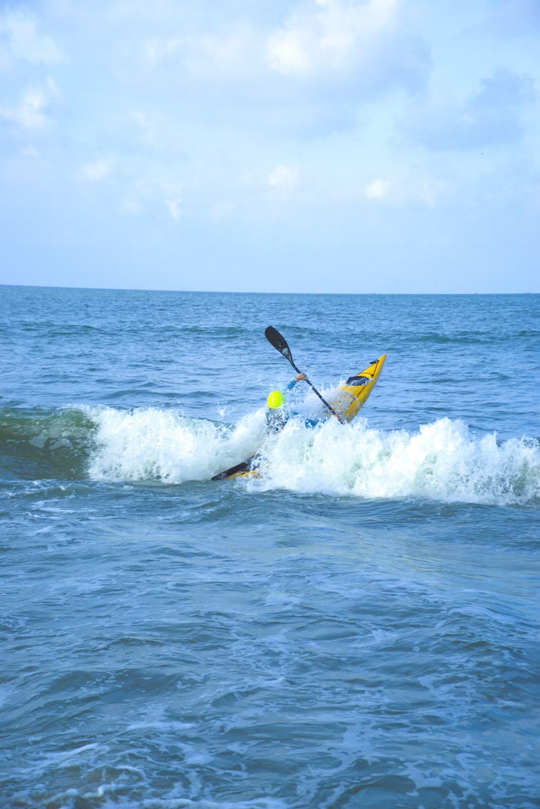 A kayaker in a yellow kayak riding the white water of a breaking wave.
