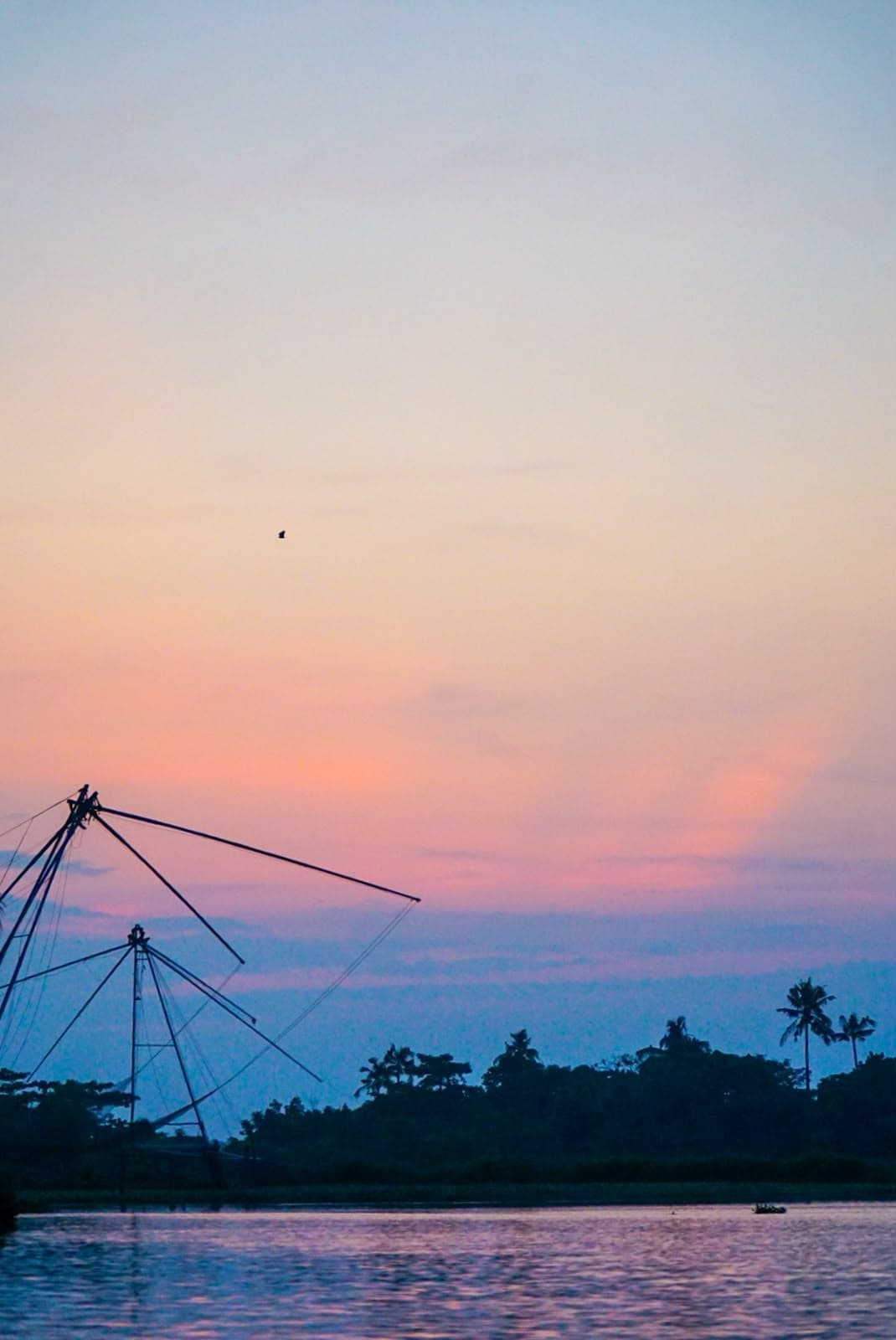 Fishing nets and palms silhouetted against a wide pink-and-blue dusk sky.