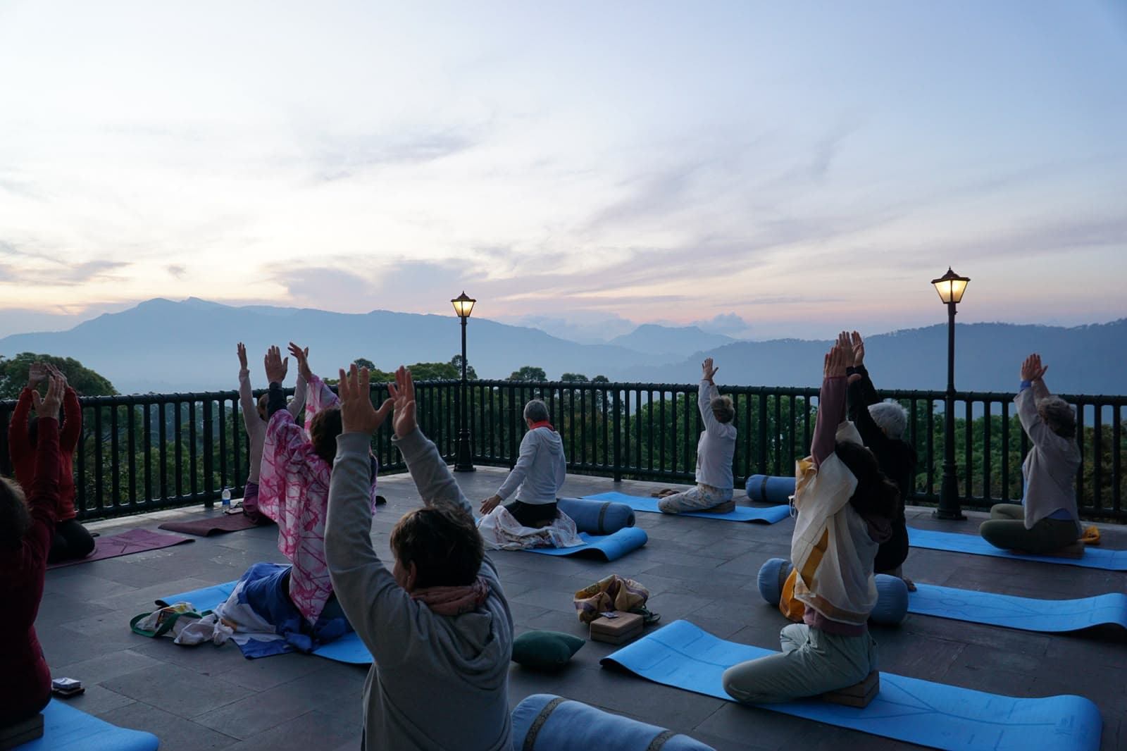 A yoga session on an open terrace at sunrise, hills fading into cloud beyond.