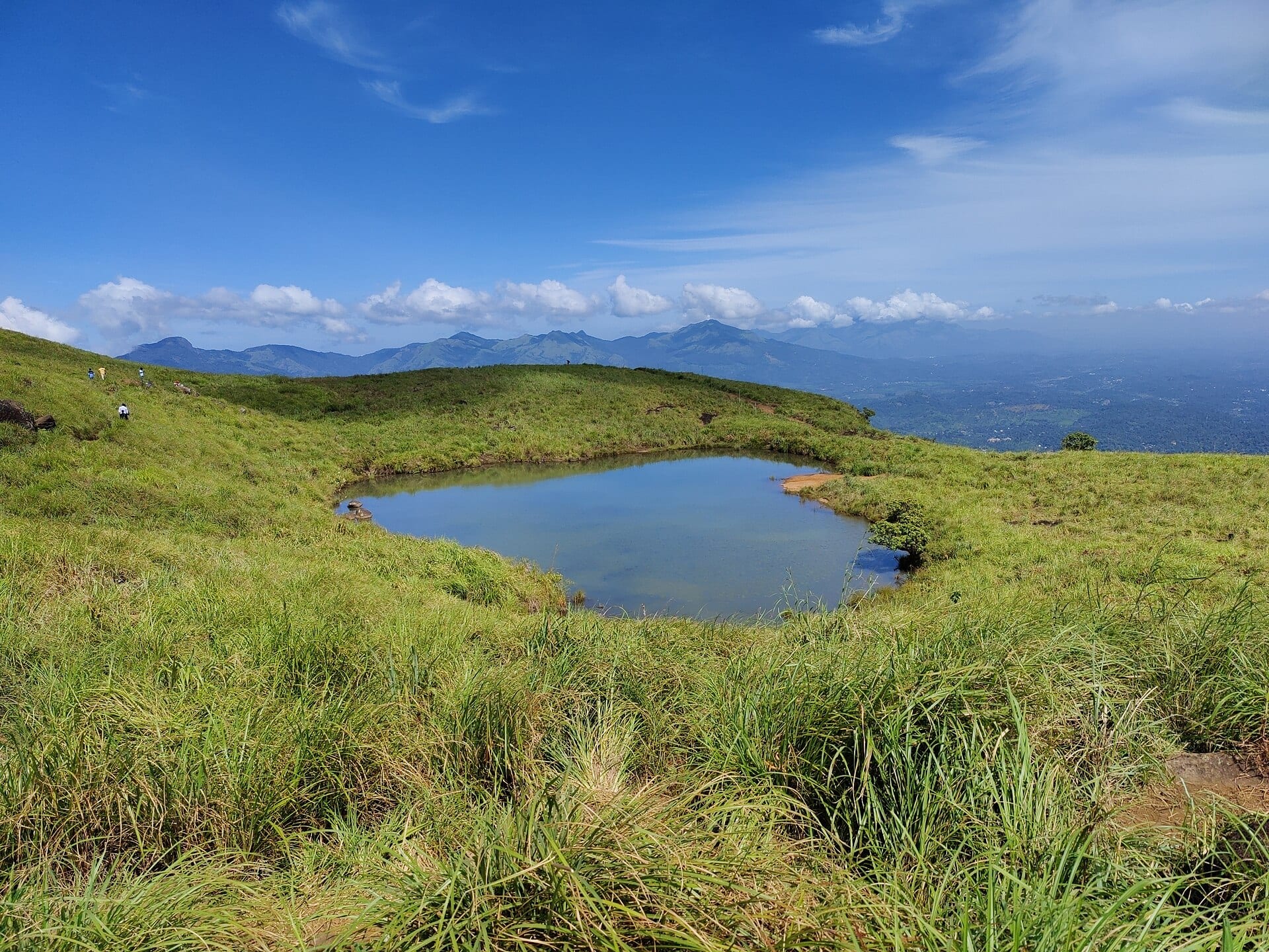 A heart-shaped lake on a grassy ridge with the Wayanad ranges behind it.