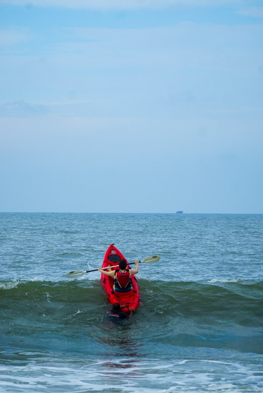 A kayaker in a red kayak paddling out through the surf.